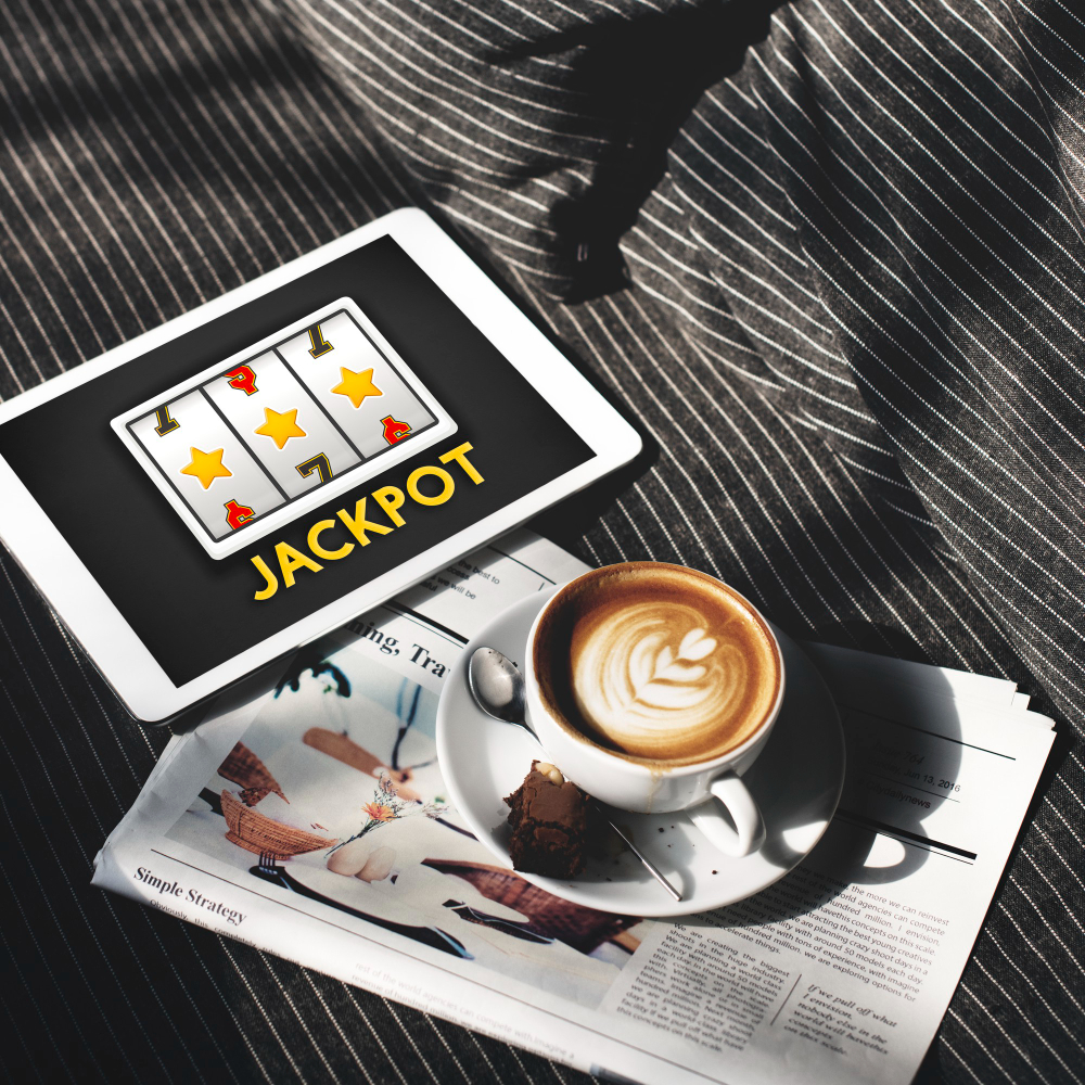 Morning coffee put on a newspaper with a tablet on the side showing a slot machine in action and a label below it saying Jackpot